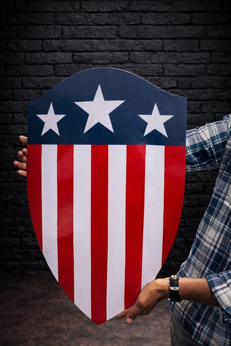 May include: A shield with a patriotic design. The top section is navy blue with three white stars. The shield features alternating red and white vertical stripes, creating a bold and iconic look. The shield is held by a person.