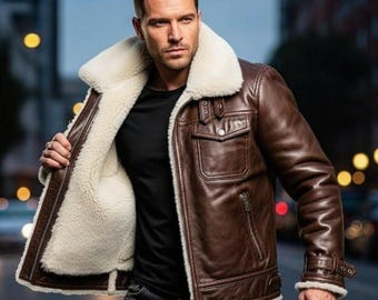 May include: A brown leather jacket with a cream-colored shearling lining and collar. The jacket features a zip closure, two chest pockets, and a buckled strap at the wrist. The jacket is a classic outerwear piece.