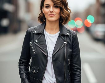 May include: A black leather motorcycle jacket with silver zippers and snaps. The jacket is worn over a white t-shirt and blue jeans. The person is standing on a city street.
