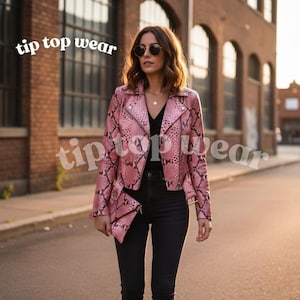 Op de afbeelding: Een roze jasje met slangenpatroon en bijpassende clutch. De jas heeft een klassieke biker-stijl met een reverskraag en asymmetrische rits. De tekst "tip top wear" is zichtbaar.