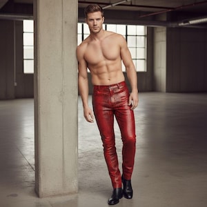 Puede incluir: Una persona lleva pantalones rojos con textura de piel de serpiente y botas negras. La persona está apoyada en un pilar de hormigón en un espacio amplio y abierto. La persona está sin camisa.