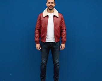 May include: A red leather jacket with a cream-colored shearling collar. The jacket is paired with a white t-shirt, dark blue jeans, and brown leather shoes. The background is a solid blue wall.
