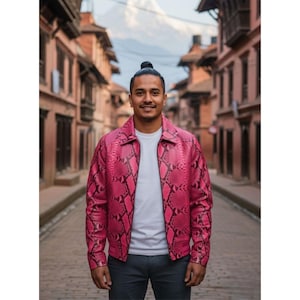Può includere: Giacca in pelle rosa acceso con motivo a pelle di serpente. La giacca ha una chiusura a zip frontale e un colletto classico. La giacca è indossata sopra una maglietta bianca e pantaloni grigio scuro. Lo sfondo mostra una strada con edifici.