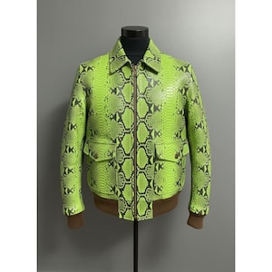 Könnte beinhalten: Eine neongrüne Jacke mit Schlangenmuster und einem braunen, gerippten Saum und Bündchen. Die Jacke hat einen Reißverschluss, zwei Vordertaschen und einen klassischen Kragen. Die Jacke wird auf einer schwarzen Schaufensterpuppe präsentiert.