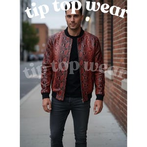Puede incluir: Chaqueta bomber con estampado de piel de serpiente roja y marrón con cuello y puños negros. La chaqueta está abrochada con una camisa negra y vaqueros grises oscuros. El texto blanco dice "tip top wear".