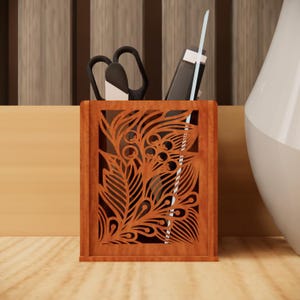 May include: A brown wooden desk tidy with a decorative floral cut-out design. It contains scissors, a pen, and a stylus. The desk tidy sits on a light brown surface.