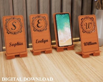 Puede incluir: Cuatro soportes de teléfono de madera con nombres e iniciales personalizados. Cada soporte es de color marrón claro y presenta un diseño decorativo alrededor de la inicial. Un soporte sostiene un teléfono inteligente. El texto "DESCARGA DIGITAL" está en la parte inferior.
