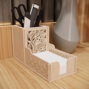 Op de afbeelding: Een lichtgekleurde houten bureau-organizer met een bloemenuitsparing. De organizer heeft vakken voor pennen, scharen en notitiepapier. Een grijze vaas staat op de achtergrond.
