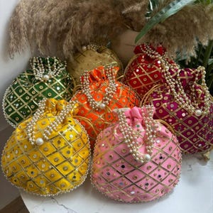 Può includere: Una collezione di borse rotonde con coulisse colorate. Ogni borsa è di un colore diverso, tra cui giallo, verde, arancione, rosa, rosso e oro. Sono decorate con finiture dorate, piccoli specchi e cordini di perle.