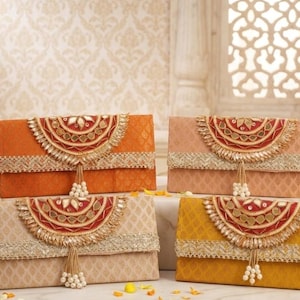May include: Four decorative clutch purses in shades of orange, peach, beige, and yellow. Each clutch features a decorative flap with red and gold embellishments, a gold trim, and a beaded tassel. The purses are rectangular in shape.