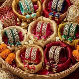 Peut inclure: Un panier en osier rempli de bracelets et de boucles d'oreilles colorés. Les bracelets sont de couleurs turquoise, bleu, rouge, vert et bordeaux, ornés de motifs floraux. Les boucles d'oreilles sont assorties, créant un ensemble vibrant.