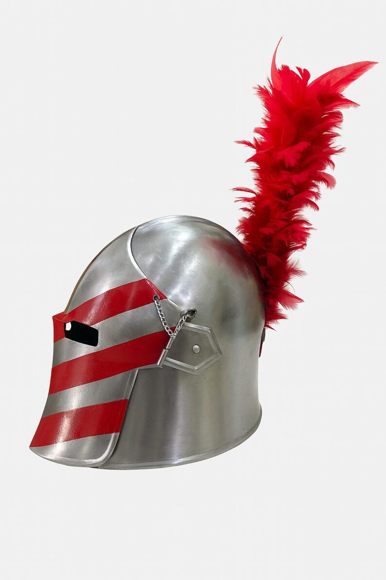May include: A silver-colored knight's helmet with red stripes on the visor and a chain detail. A large plume of red feathers extends from the top of the helmet. The helmet is likely made of metal and is designed for protection.