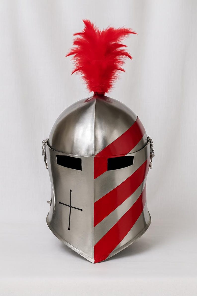 May include: A silver-colored medieval helmet with red stripes and a red feather plume. The helmet has a cross design on the front and eye slits. Chains hang from the sides.