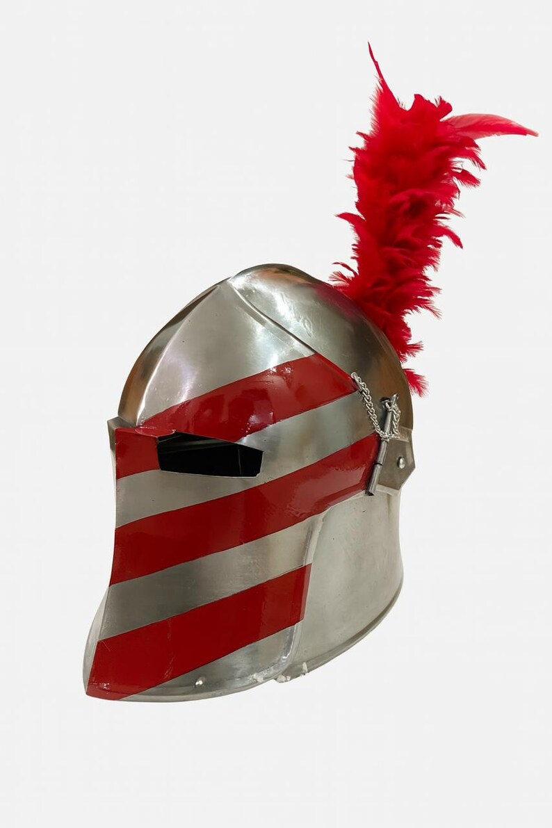 May include: A silver-colored medieval helmet with red stripes and a red plume. The helmet has a visor with a narrow eye slit and a chain detail. The red stripes are painted across the front and sides of the helmet.