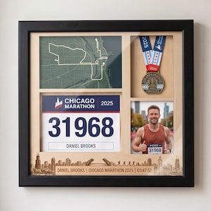 May include: A black shadow box frame containing a Chicago Marathon 2025 display. It features a green map, a race medal with a blue and white ribbon, a race bib numbered 31968 for Daniel Brooks, and a photo of a runner in a brown tank top.