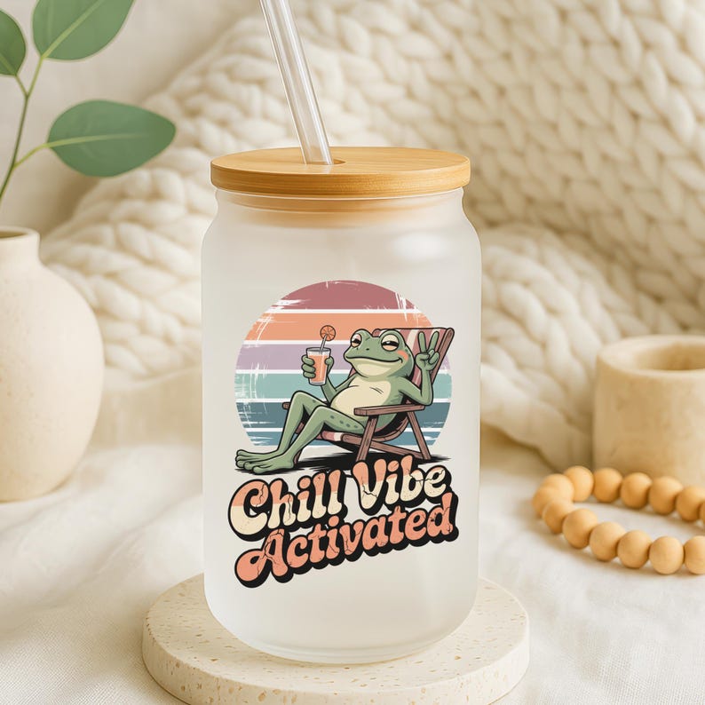 Pode incluir: Copo de vidro fosco em forma de lata com tampa e canudo de bambu. O copo apresenta um gr&aacute;fico de um sapo de desenho animado relaxando em uma cadeira com uma bebida, o texto "Chill Vibe Activated" est&aacute; abaixo.
