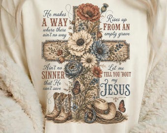 May include: A cream-colored t-shirt featuring a graphic of a wooden cross adorned with colorful flowers, a pair of cowboy boots, a cowboy hat, and a butterfly. The text reads: He makes A WAY where there ain't no way, Rises up FROM AN empty grave, Ain't no SINNER that He can't save, Let me TELL YOU 'bout my JESUS.