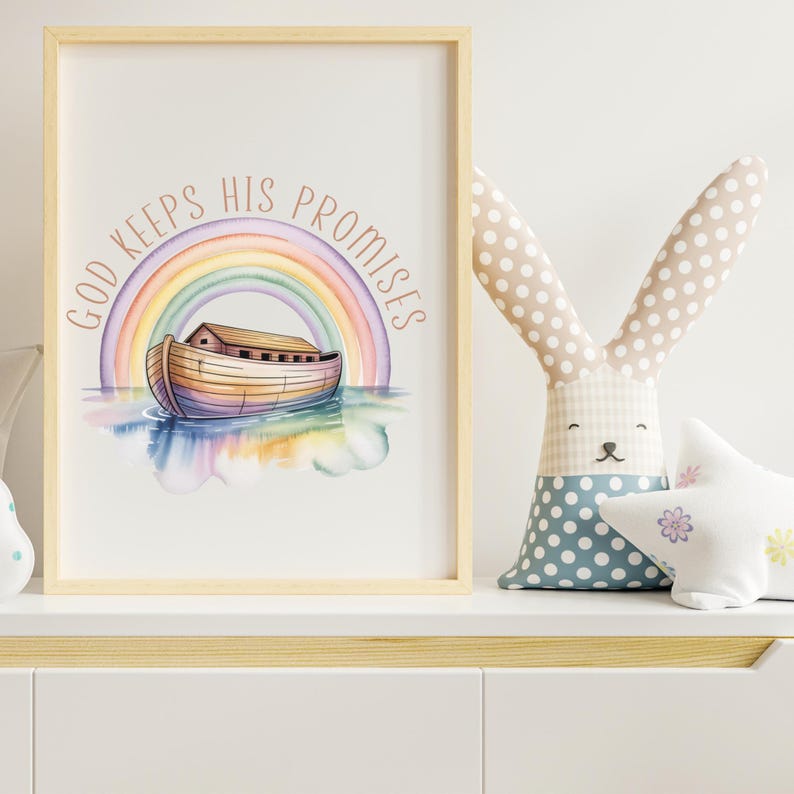 Puede incluir: Una impresi&oacute;n en acuarela enmarcada con un arco&iacute;ris, el Arca de No&eacute; y el texto "GOD KEEPS HIS PROMISES" en un dise&ntilde;o circular. Un conejito de peluche con orejas de lunares y una almohada en forma de estrella est&aacute;n en un estante blanco.