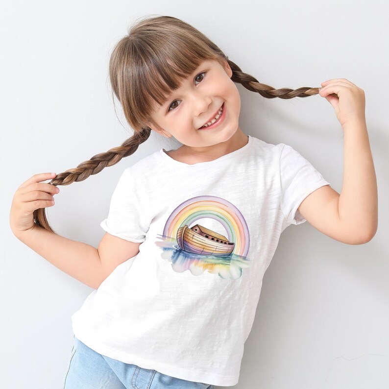 Puede incluir: Una camiseta blanca con una ilustraci&oacute;n de acuarela del Arca de No&eacute; y un arco&iacute;ris. El arca se representa flotando sobre el agua, con un arco&iacute;ris colorido arque&aacute;ndose sobre ella. La camiseta la lleva una persona joven con el pelo casta&ntilde;o en trenzas.