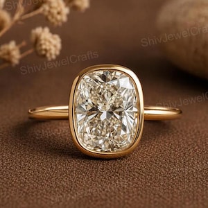 May include: A gold ring featuring a large, cushion-cut, champagne-colored center stone held in a smooth bezel setting. The band is thin, polished, and circular, providing a clean, continuous look that highlights the faceted gemstone.
