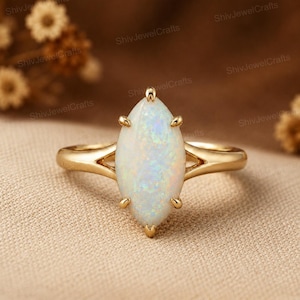Puede incluir: Un anillo de oro amarillo pulido con un ópalo de talla marquesa. El ópalo central muestra destellos iridiscentes en azul, verde y naranja. La piedra está asegurada por seis pequeñas garras de oro y el aro presenta un diseño dividido.