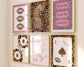May include: A collection of six framed art prints with gold frames. The prints feature leopard print, pink, and white designs. The prints include images of lips, a leopard, playing cards, and the text "LUCKY YOU, LUCKY ME, LUCKY US".