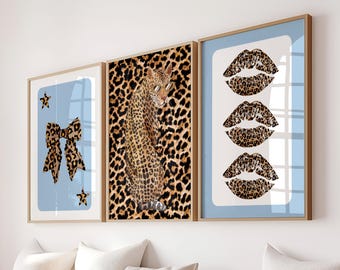 May include: Three framed art prints with a light blue background. One print features a leopard print bow and stars. Another shows a leopard with sunglasses. The third print displays three sets of leopard print lips.