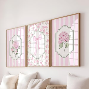 May include: Three framed floral art prints. Each print features a watercolor design of pink hydrangeas or a pink bow on a white and pink striped or floral background. The frames are a light brown color.
