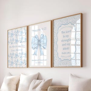 Può includere: Un set di tre stampe artistiche da parete incorniciate con motivi floreali azzurri e testo. La stampa a sinistra riporta His Mercies Are New Every Morning. Quella centrale mostra un grande fiocco azzurro e Proverbs 31:25. Quella a destra riporta The Lord is my strength and my shield Psalm 28:7.