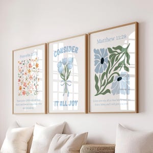 Può includere: Tre stampe da parete incorniciate con bordi in legno chiaro. La stampa a sinistra presenta un motivo floreale e Proverbs 3:5-6. Quella centrale mostra fiori blu con il testo CONSIDER IT ALL JOY. Quella a destra mostra fiori e Matthew 11:28.