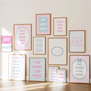 May include: A collection of eleven rectangular wall art prints in wooden frames, featuring pastel pink and blue color schemes with various humorous text phrases like Get Naked, You Look Good, Please Wash Your Hands, and Are You Pooping.