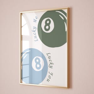 May include: A framed print featuring two stylized eight-ball designs in blue and green, with the text "Lucky Me" and "Lucky You" in a cursive font. The frame is gold.