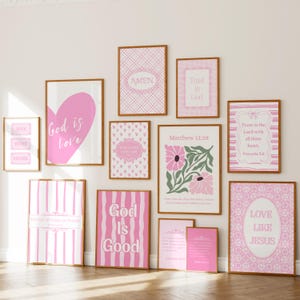 May include: A gallery wall set of eleven framed art prints featuring pink and white color schemes. The prints display various religious phrases including God is love, Amen, Trust in God, Matthew 11:28, and Love like Jesus, alongside floral and geometric patterns.