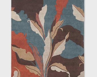 May include: A rectangular area rug with a botanical design. The rug features a pattern of large leaves in shades of beige, brown, and rust against a teal and dark brown background. The rug's design is abstract and modern.