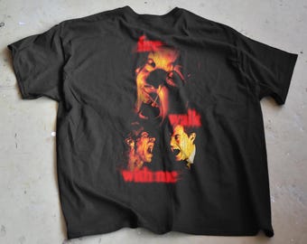 Może przedstawiać: Czarny t-shirt z grafiką przedstawiającą trzy twarze w odcieniach czerwieni i żółci. Tekst "fire walk with me" jest wydrukowany na czerwono. Koszulka wykonana jest z miękkiego materiału.
