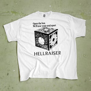 Könnte beinhalten: Weißes T-Shirt mit einer schwarz-weißen Grafik des Puzzle-Würfels aus dem Film Hellraiser. Das Shirt trägt den Text "Open the box, We'll tear your soul apart" über dem Würfel und "HELLRAISER" darunter.