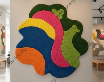 May include: A large, abstract rug with a colorful design. The rug features a combination of orange, blue, yellow, pink, and green shapes. The rug is displayed on a white wall in a gallery setting.