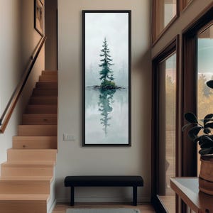 May include: A framed landscape art print depicts a solitary evergreen tree on a small island reflected in calm water. The artwork features a muted color palette of greens, blues, and grays, creating a serene and natural scene. The artwork is displayed on a wall.