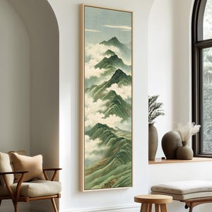 May include: A tall, vertical framed wall art piece featuring a landscape painting of layered green mountain peaks partially obscured by soft white clouds under a pale sky. The artwork is enclosed in a light-colored wooden frame.