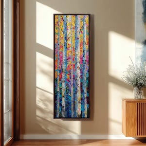 May include: A vertical abstract painting of birch trees with a colorful palette. The artwork features vertical strokes of blue, yellow, pink, and purple, creating a textured effect. The painting is framed in a dark brown wooden frame.