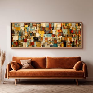 Könnte beinhalten: Ein rechteckiges Wandbild mit einem Gitter aus bunten Quadraten in Gelb-, Orange-, Rot-, Blau- und Weißtönen, gerahmt in hellem Holz. Darunter steht ein langes, einfarbiges orangefarbenes Samtsofa mit zwei passenden Zierkissen.