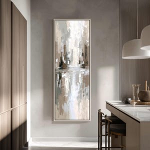 May include: Abstract art print in a vertical rectangular frame. The artwork features a cityscape in neutral tones of white, grey, and brown, with a reflective water-like effect at the bottom. The painting is displayed on a light grey wall.