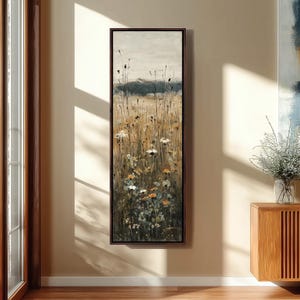 Puede incluir: Una pieza de arte mural enmarcada, alta y rectangular, que presenta una pintura impresionista de un campo de flores silvestres y hierbas altas en tonos dorados, marrones, blancos y verde oscuro bajo un cielo nublado.