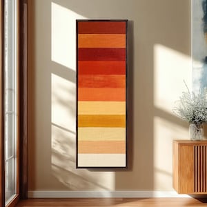 May include: A tall, rectangular wall art piece featuring a series of horizontal stripes in a gradient of warm colors, transitioning from deep dark red at the top to light cream and off-white at the bottom, enclosed in a thin dark frame.