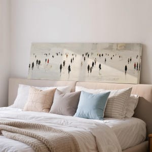 May include: A large rectangular canvas art piece depicting a crowd of people in black and red against a light background hangs above a bed. The bed is made with white linens and several decorative pillows in neutral colors.