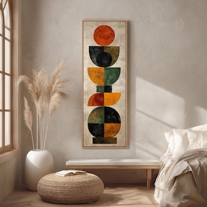 Può includere: Opera d'arte geometrica astratta da parete in una cornice rettangolare verticale. L'opera presenta una serie di forme impilate in arancione, nero, verde e giallo. L'opera è esposta in una stanza dai toni neutri con una finestra e un pouf intrecciato.