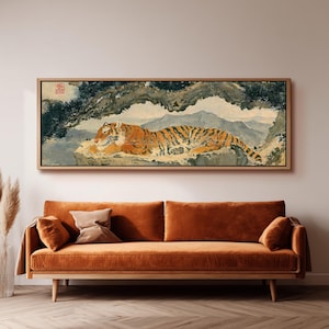Puede incluir: Una pieza de arte mural rectangular en un marco de madera clara que presenta una pintura de un tigre naranja y negro descansando sobre una repisa rocosa bajo un pino, con montañas distantes al fondo y un pequeño sello cuadrado rojo arriba.