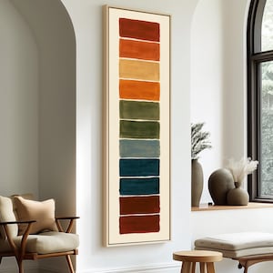 May include: A tall, vertical framed wall art piece featuring a series of ten stacked, rectangular color blocks in shades of deep red, orange, golden yellow, olive green, sage, slate blue, dark teal, navy, and dark brown on a cream background.
