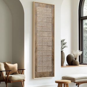 May include: A rectangular, framed wall art piece with a textured, grid-like pattern in shades of brown and beige. The artwork is displayed vertically on a white wall, adding a touch of modern decor to the room. The frame is a light brown color.