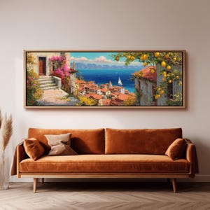 Può includere: Un dipinto paesaggistico rettangolare in una cornice di legno chiaro che raffigura un villaggio costiero con tetti in terracotta, un mare blu, una barca a vela e un albero di limoni con frutti gialli in primo piano, appeso sopra un lungo divano in velluto arancione.